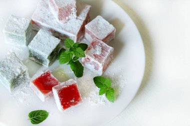 Türk lokumu. Lokum, renkli, aromalı, pudra şekeriyle kaplanmış jöle aromalı şekerler beyaz bir masada servis edilir. Nane yaprakları dekorasyon.