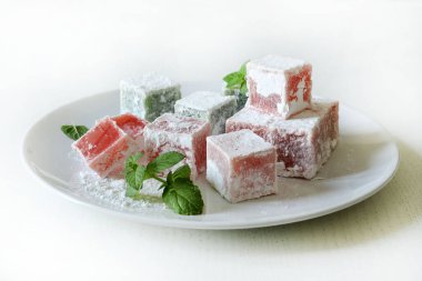 Türk lokumu. Lokum, renkli, aromalı, pudra şekeriyle kaplanmış jöle aromalı şekerler beyaz bir masada servis edilir. Nane yaprakları dekorasyon.