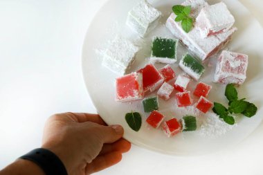Türk lokumu. Lokum, renkli, aromalı, pudra şekeriyle kaplanmış jöle aromalı şekerler beyaz bir masada servis edilir. Nane yaprakları dekorasyon.