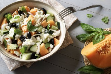 Lezzetli kavun, peynir, zeytin, salatalık aromalı salata ve gri ahşap arka planda taze fesleğen yaprağı. Hafif bir yaz yemeği..