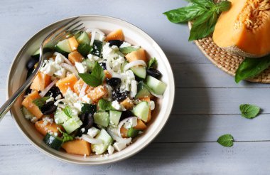 Lezzetli kavun, peynir, zeytin, salatalık aromalı salata ve gri ahşap arka planda taze fesleğen yaprağı. Hafif bir yaz yemeği..