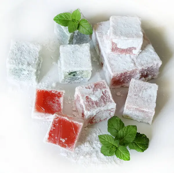 Türk lokumu. Lokum, renkli, aromalı, pudra şekeriyle kaplanmış jöle aromalı şekerler beyaz bir masada servis edilir. Nane yaprakları dekorasyon.