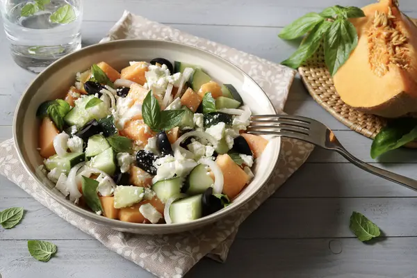 Lezzetli kavun, peynir, zeytin, salatalık aromalı salata ve gri ahşap arka planda taze fesleğen yaprağı. Hafif bir yaz yemeği..