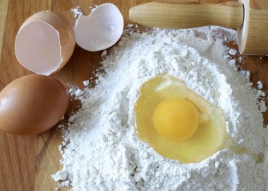 Hamur yapmak için gerekli malzemeler. Kırık yumurtalı beyaz un, bütün bir yumurta, yumurta kabuğu ve ahşap bir arka planda merdane. Tam üstte.