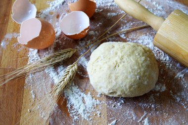 Pişirmeye hazır ev yapımı taze hamur, merdane, yumurta kabuğu ve un ahşap arka planda buğday kulağı. Tam üstte.