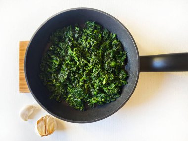 Siyah bir tavada lezzetli ıspanak ve beyaz bir masada sarımsak. Sağlıklı bir yaşam tarzı. Vejetaryen yemeği. Genel Görünüm.