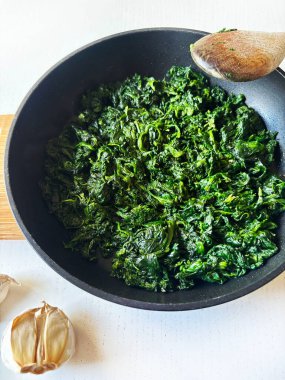 Siyah bir tavada lezzetli ıspanak ve beyaz bir masada sarımsak. Sağlıklı bir yaşam tarzı. Vejetaryen yemeği. Genel Görünüm.