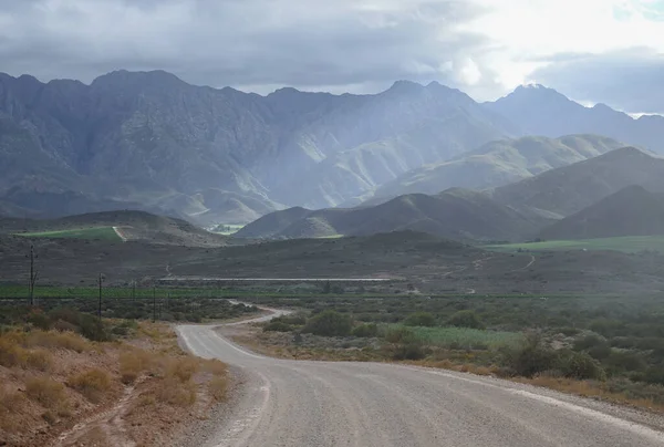 Arka planda sisli bulutlar ve ön planda bir yol olan dağ manzarası