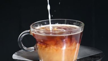 Şeffaf bir fincan kahveye dökülen sütün yavaş çekim videosu.