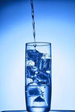 Bardaktaki su, mavi arkaplanda su sıçraması. Kapat.