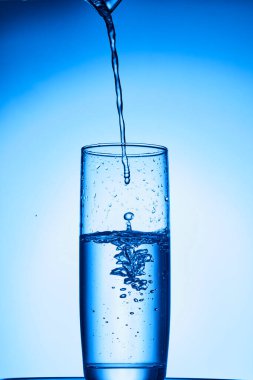 Su bardağa sıçrıyor mavi bir sıvının arka planında bir damla suyla