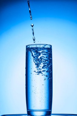 Beyaz zemin üzerinde mavi sıvı olan bir bardak su.