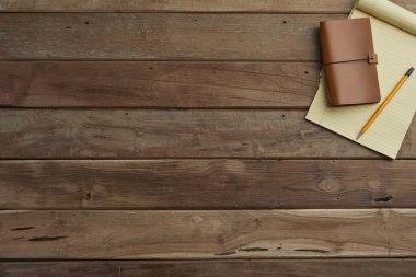 Boş defter, not defteri, kalem, kahve fincanı, tahta masa üzerinde bitki ve bardakla ofis işyerinin üst görüntüsü.