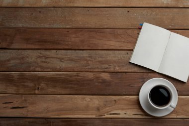 Boş beyaz defter, bir fincan kahve ve tahta yüzeyde kalem.
