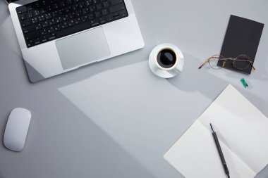 Düz konumda dizüstü bilgisayar, kahve ve kırtasiye malzemesi var. iş yeri