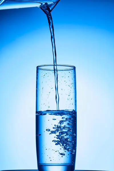 Mavi zemin üzerinde su bardağı olan su sıçraması..