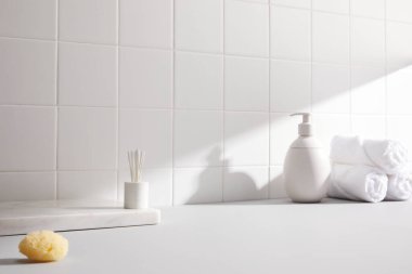 Banyo içi beyaz havluyla beyaz bir masa üzerinde ayna ve sabun şişesi..