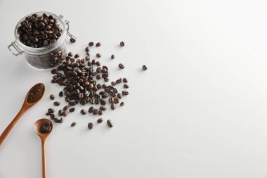 Kahve çekirdekleri fincanda, kaşık da beyaz arka planda.