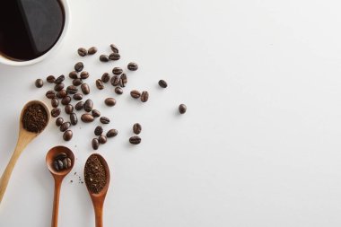 Beyaz arka planda kaşık ile beyaz fincanda kahve çekirdekleri