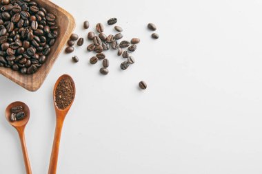 Beyaz fincanda kahve çekirdekleri ve beyaz grupta izole edilmiş ahşap kepçe.