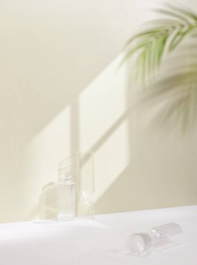 beyaz bir parfüm şişesi, bir bardak su ve beyaz bir çiçek, gün ışığında ahşap bir masada..