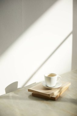 Ilık güneş ışığı, çimen yapraklarından gölgeler, masa üstünde vazo ve fincanlar gibi çeşitli nesnelerin olduğu bir oda.