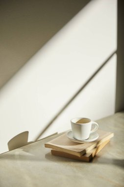 Ilık güneş ışığı, çimen yapraklarından gölgeler, masa üstünde vazo ve fincanlar gibi çeşitli nesnelerin olduğu bir oda.