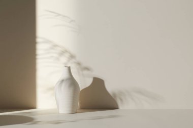 Ilık güneş ışığı, çimen yapraklarından gölgeler, masa üstünde vazo ve fincanlar gibi çeşitli nesnelerin olduğu bir oda.