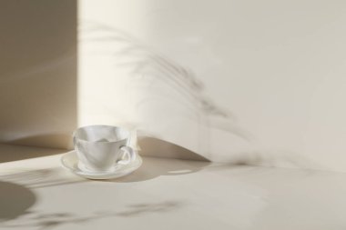 Ilık güneş ışığı, çimen yapraklarından gölgeler, masa üstünde vazo ve fincanlar gibi çeşitli nesnelerin olduğu bir oda.