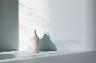 Ilık güneş ışığı, çimen yapraklarından gölgeler, masa üstünde vazo ve fincanlar gibi çeşitli nesnelerin olduğu bir oda.