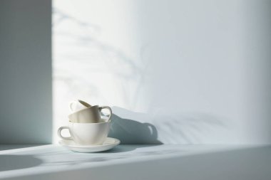 Ilık güneş ışığı, çimen yapraklarından gölgeler, masa üstünde vazo ve fincanlar gibi çeşitli nesnelerin olduğu bir oda.