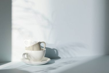 Ilık güneş ışığı, çimen yapraklarından gölgeler, masa üstünde vazo ve fincanlar gibi çeşitli nesnelerin olduğu bir oda.