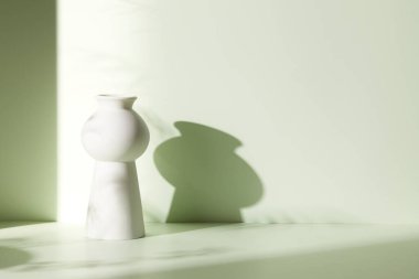 Ilık güneş ışığı, çimen yapraklarından gölgeler, masa üstünde vazo ve fincanlar gibi çeşitli nesnelerin olduğu bir oda.