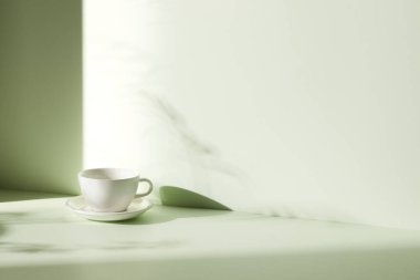 Ilık güneş ışığı, çimen yapraklarından gölgeler, masa üstünde vazo ve fincanlar gibi çeşitli nesnelerin olduğu bir oda.