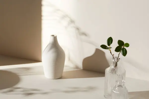 Ilık güneş ışığı, çimen yapraklarından gölgeler, masa üstünde vazo ve fincanlar gibi çeşitli nesnelerin olduğu bir oda.