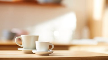 Beyaz fayans duvarlı güneşli bir mutfak, ahşap bir masa ve lavabo..