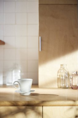 Beyaz fayans duvarlı güneşli bir mutfak, ahşap bir masa ve lavabo..