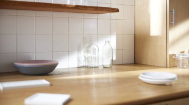 Beyaz fayans duvarlı güneşli bir mutfak, ahşap bir masa ve lavabo..