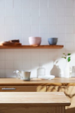 Beyaz fayans duvarlı güneşli bir mutfak, ahşap bir masa ve lavabo..