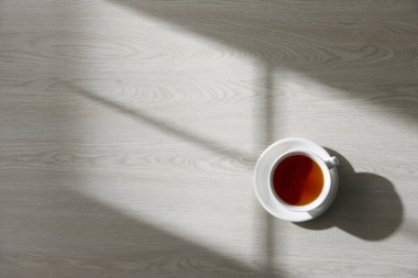 Bardak ve çay ahşap bir masada, doğal ışık çayırdan içeri akıyor..