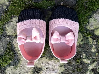 Cute little baby shoes pink and black color on plaster and moss plants background clipart