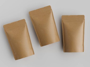 Üç açık kahverengi kraft kağıt kesesi düz açık gri bir yüzey üzerinde duruyor. Keseler üst üste binerek dikdörtgen şekillerini ve mühürlü kenarlarını gösteriyorlar. Resim iyi aydınlatılmış, ambalajın net bir görünümü oluşturuluyor.