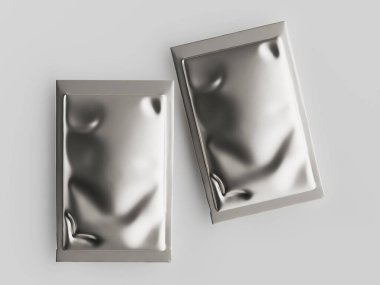 İki dikdörtgen, metalik gri gıda paketi yukarıdan aşağıya doğru bir perspektiften sergilenir. Paketler kırışmış, kırışmış yüzeyleri yansıtıcı nitelikte. Arka plan basit, nötr gri, stüdyo ortamını gösteriyor. Gösteri için ideal.