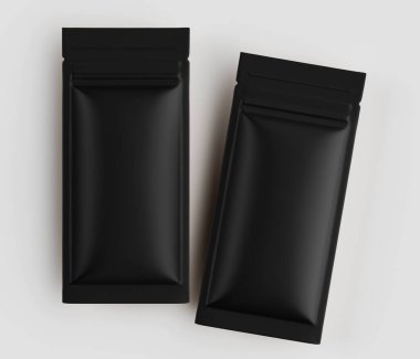 İki siyah, mat, dikdörtgen keseler ya da paketler açık gri bir yüzeyde yan yana uzanıyorlar. Torbaların pürüzsüz ve kabartmalı bir dokusu var. Görüntü yüksek açılı, yukarıdan çekilmiş. Prodüktörün tasarımı ve ambalajını vurgular