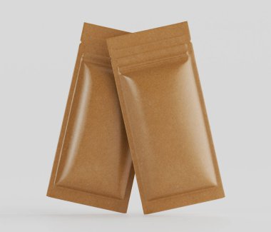 Açık kahverengi, dikdörtgen, folyo kaplı iki kese tarafsız bir arkaplanda sergileniyor. Kese, bir gıda ürününün tek porsiyonları için gibi görünüyor, muhtemelen bir aperatif veya baharat karışımı. Işık bir iç mekan olduğunu gösteriyor, muhtemelen bir stu.