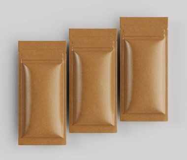 Açık kahverengimsi, neredeyse bej renkli üç paket gıda ürünü, tarafsız gri bir arkaplana karşı genel bir çekimde sunuluyor. Paketler dikdörtgen, düz ve pürüzsüz, kağıt benzeri bir malzemeden yapılmış gibi görünüyor. 