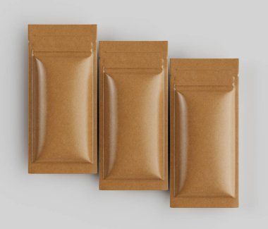 Üç dikdörtgen, açık kahverengi kesesi, parlak bir maddeden yapılmış gibi görünüyor, nötr açık gri arkaplanda yatay bir sırada düzenlenmiştir. Keselerin pürüzsüz, hafif yansıtıcı bir yüzeyi ve fermuar tarzı bir kapanışı var. Işıklandırma iyi.