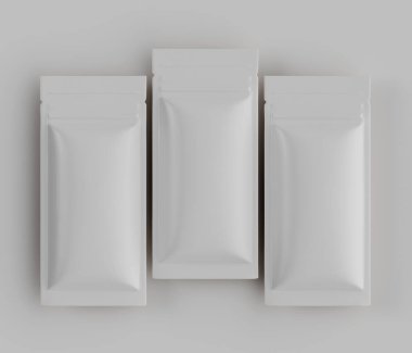 Üç özdeş, açık gri, dikdörtgen kesesi nötr açık gri arka planda yatay bir sırada dizilmiştir. Kese pürüzsüz, hafif parlak bir maddeden yapılmış gibi görünüyor. Aydınlatma düz ve tepede, açık gölgeler yaratıyor, ve