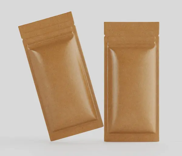 Açık kahverengimsi, dikdörtgen, folyoyla mühürlenmiş iki kese düz gri bir zeminde sunuluyor. Kese yiyecek ambalajı gibi görünüyor, muhtemelen aperatifler veya baharatlar için. Bir stüdyo ortamında tasvir ediliyorlar, pürüzsüz, hatta aydınlatmalı.