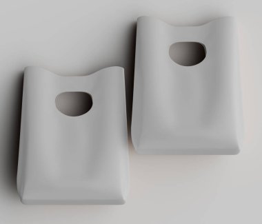 Yüksek açılı, tepeden bakıldığında iki tane açık gri, basit çanta gösteriliyor. Torbaların düz, pürüzsüz bir dokusu ve tepesine yakın dairesel bir kesiği var. Muhtemelen esnek bir malzemeden yapılmış, muhtemelen plastik ya da kağıttan. Görüntü b şeklinde alınır.